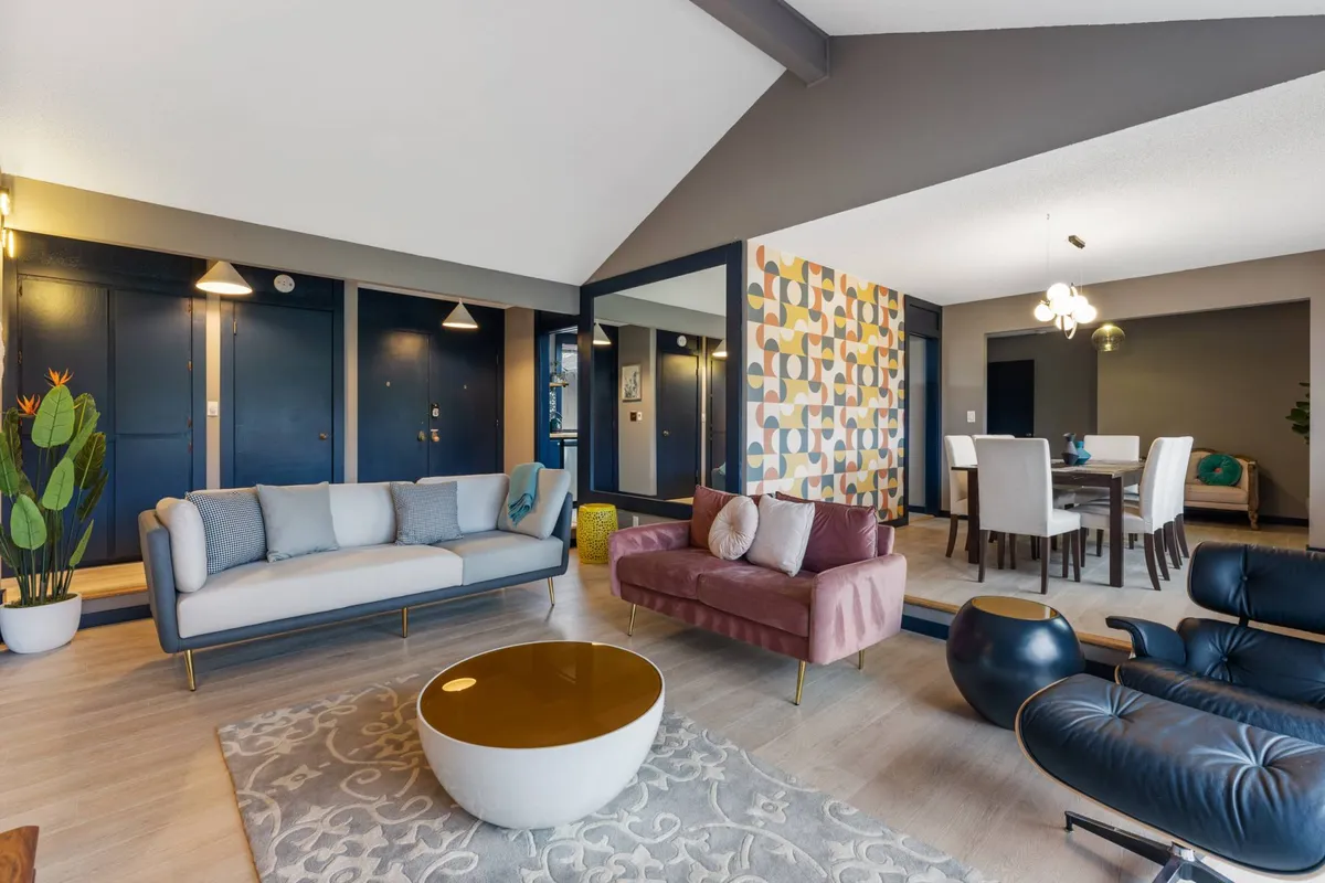 Featuring a cozy sofa, accent chairs, a round coffee table, and a dining table set against a colorful accent wall, this image showcases a space ideal for entertaining and family gatherings. The room exudes warmth, vibrancy, and comfort, with furnishings arranged to encourage conversation and relaxation.