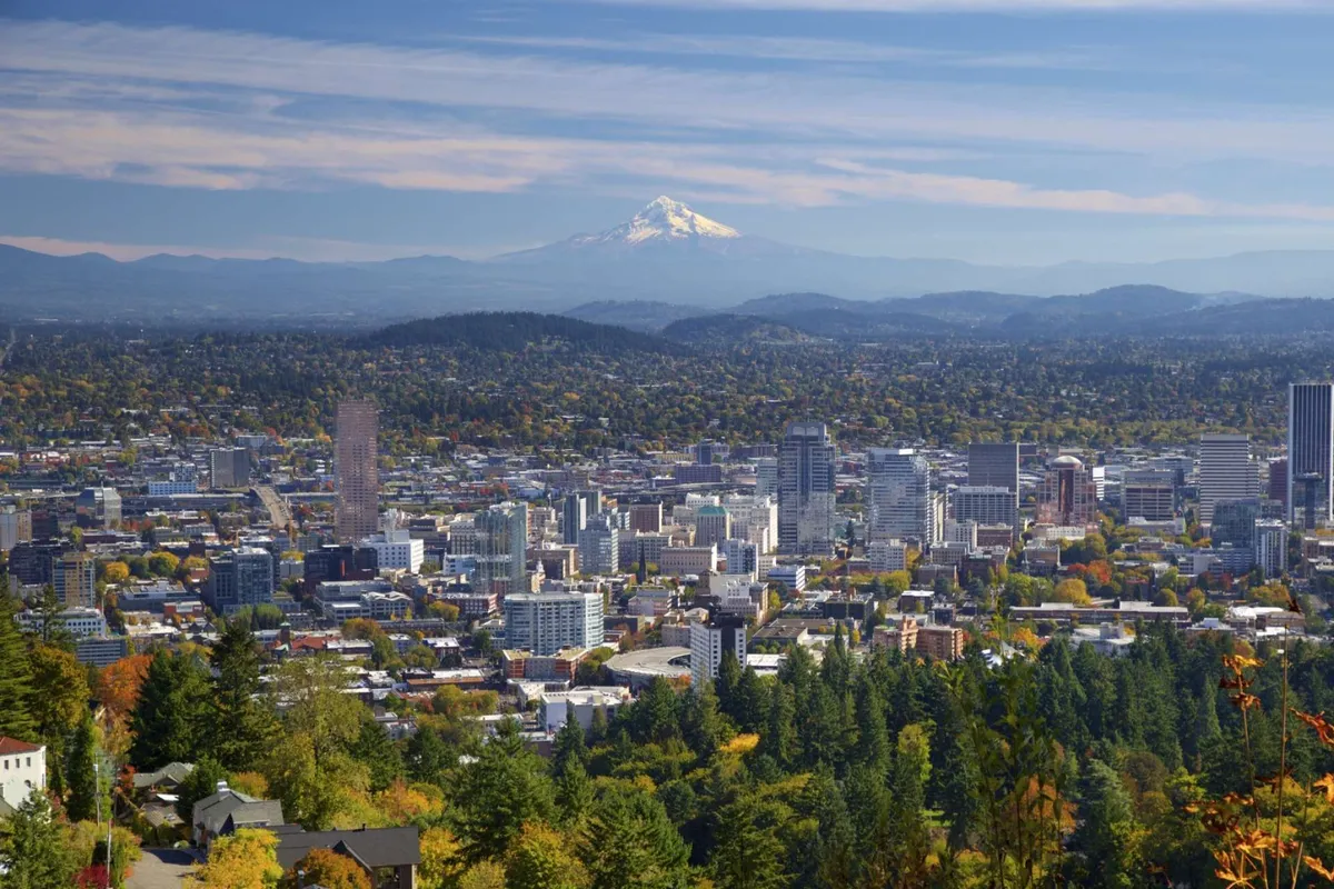 This view-focused image captures Mount Hood rising above the Portland downtown skyline, set against vibrant fall foliage and green hills. The scene exudes adventure and possibility, highlighting both urban excitement and the allure of natural beauty that surrounds the area.