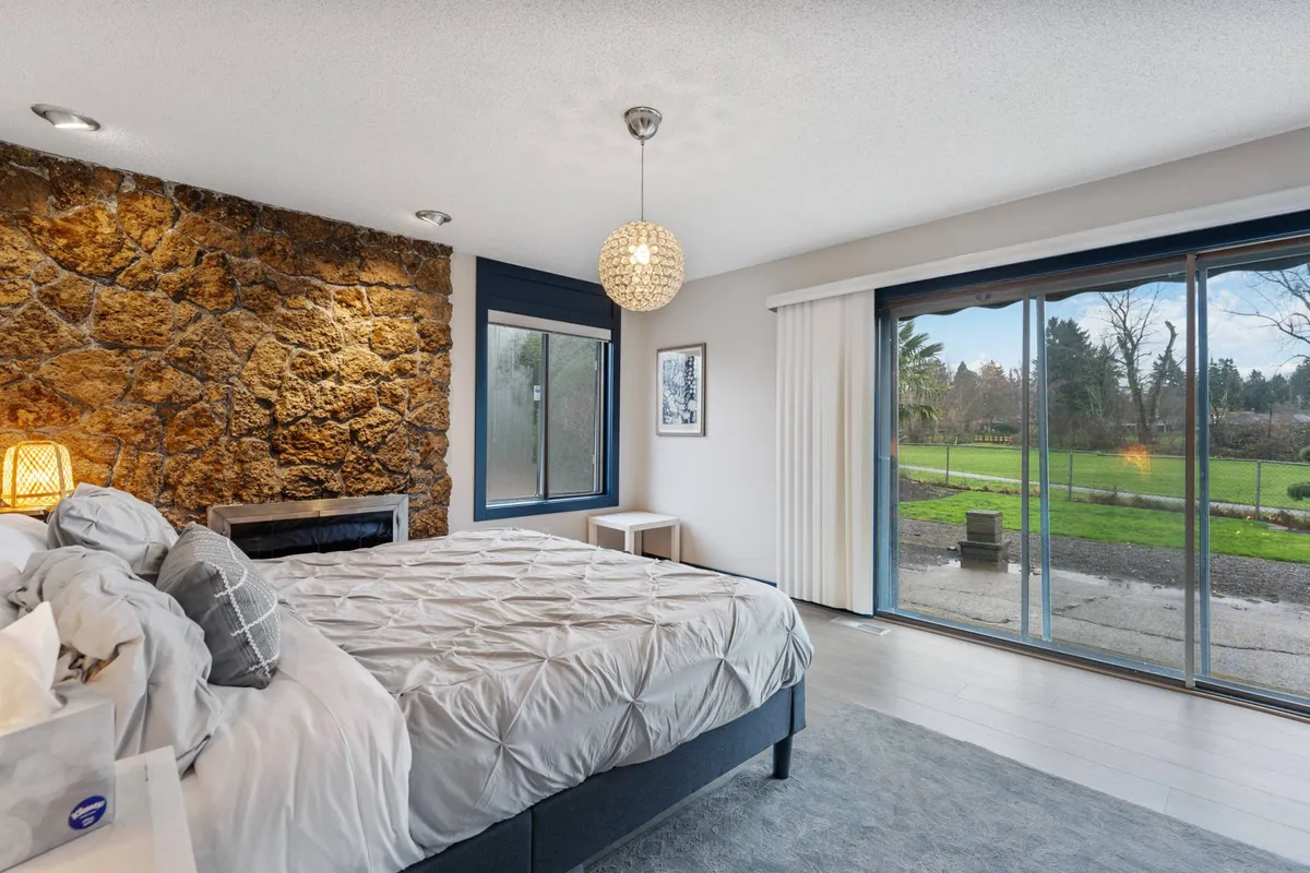 This image showcases a bedroom with a stone accent wall, a large window letting in natural light, and a bed dressed in plush bedding. The combination of textures and the calm color palette create a soothing environment ideal for relaxation.