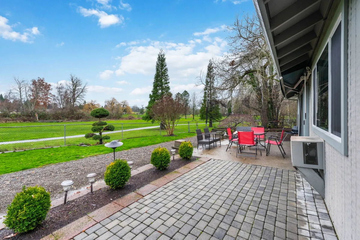 A tranquil view of a fenced backyard with a comfortable patio seating area, well-kept lawn, and landscaped garden beds. The setting is serene and feels private, ideal for unwinding or hosting an outdoor meal, with the fencing ensuring a secure space for children and pets.