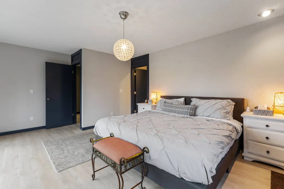 This image features a bed with a quilted cover, decorative pendant light, nightstands with lamps, and a bench at the foot of the bed. The overall atmosphere is cozy and serene, with soft lighting and calming colors that invite relaxation and restful sleep.