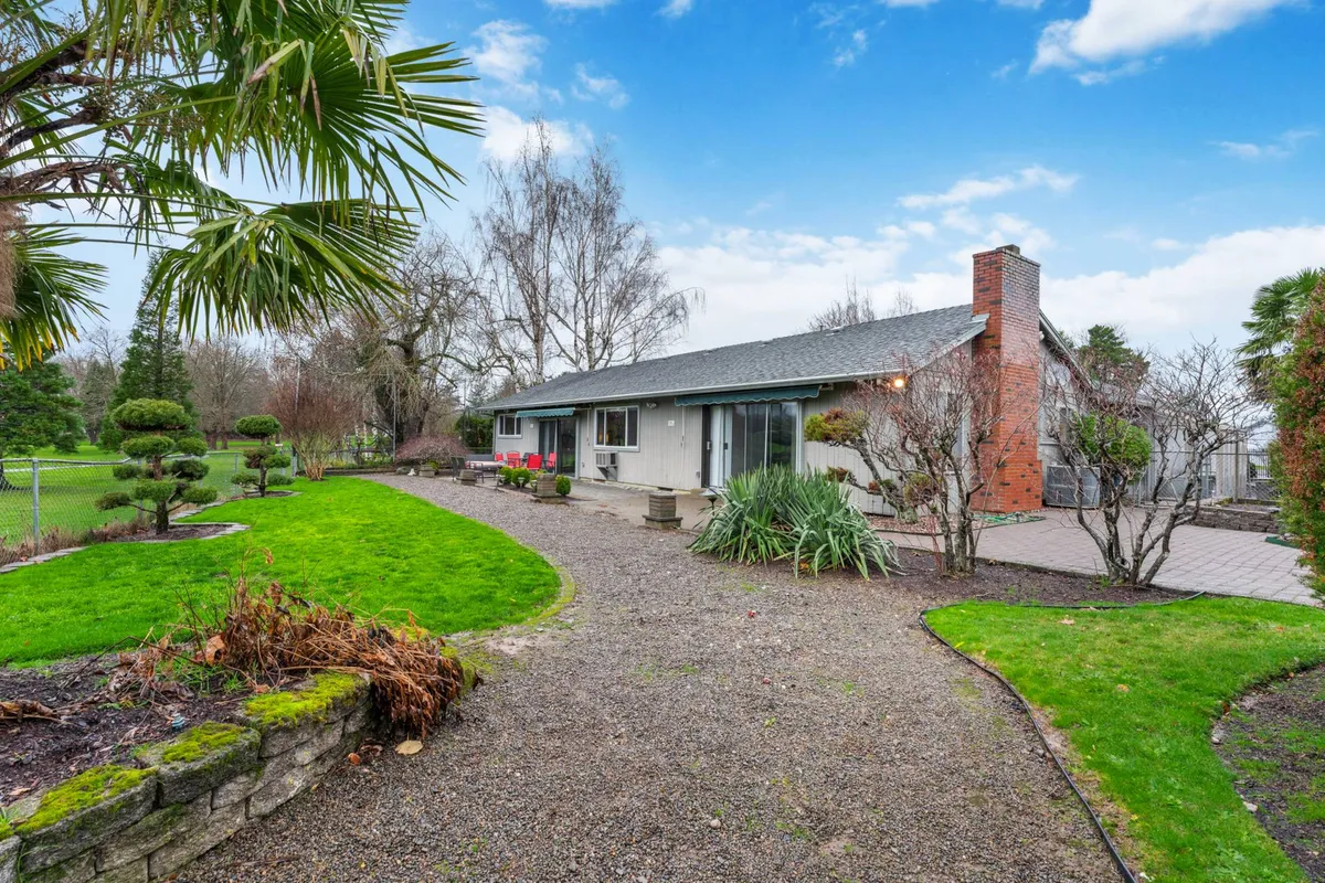 This image captures the home's facade, a patio pathway, and lush garden areas framed by a tree line. The patio space suggests a spot to sip coffee and watch the world—or golfers—go by, directly aligning with the section’s narrative.