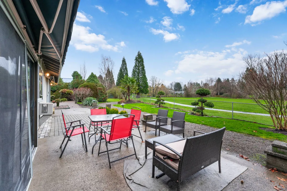 A sun-drenched patio with an inviting outdoor seating area overlooks a lush green lawn. Decorative shrubs and mature trees line the backyard, providing both beauty and privacy. The patio offers ample space for dining, relaxing, and social gatherings, while the open lawn is perfect for pets and kids to play safely.